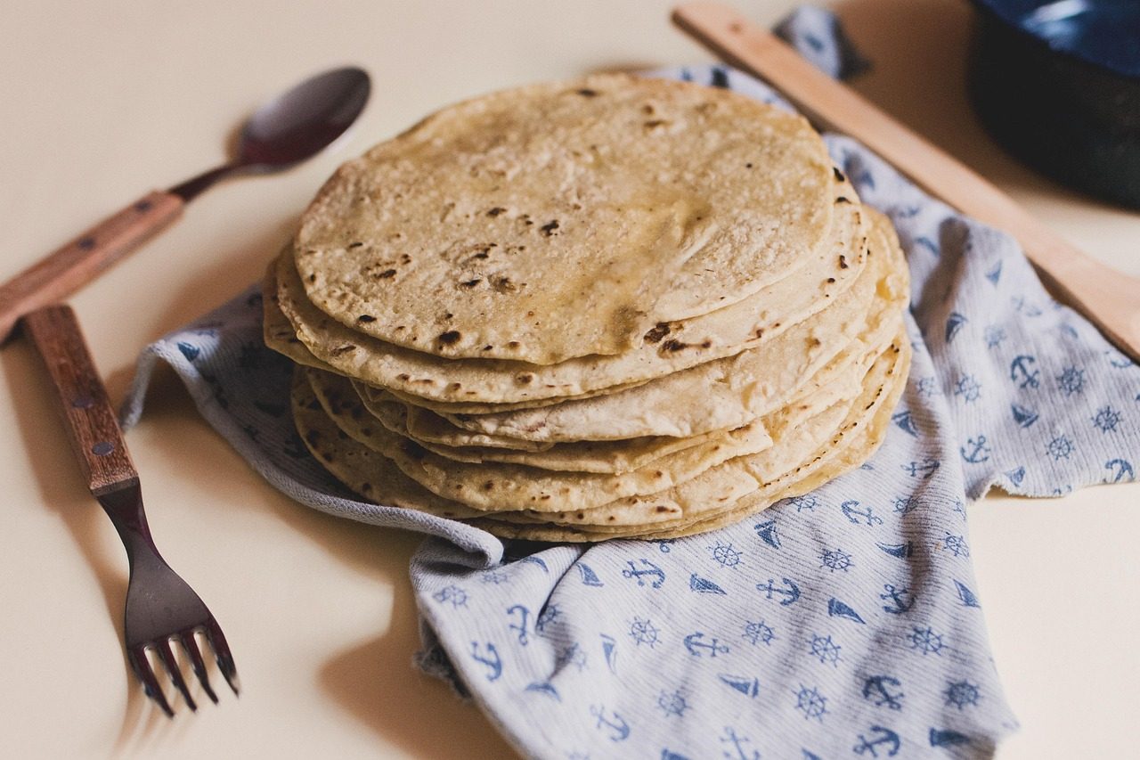 Stack of whole wheat tortillas with wooden utensils on patterned cloth